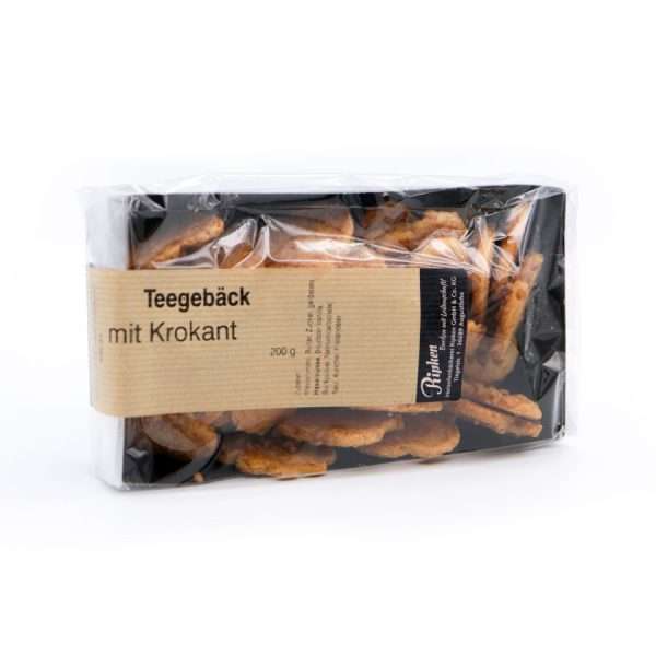 Eine Packung Teegebäck mit Krokant vor weißem Hintergrund. Die transparente Verpackung gibt den Blick auf die Kekse im Inneren frei. Das Etikett ist beige mit schwarzem Text.
