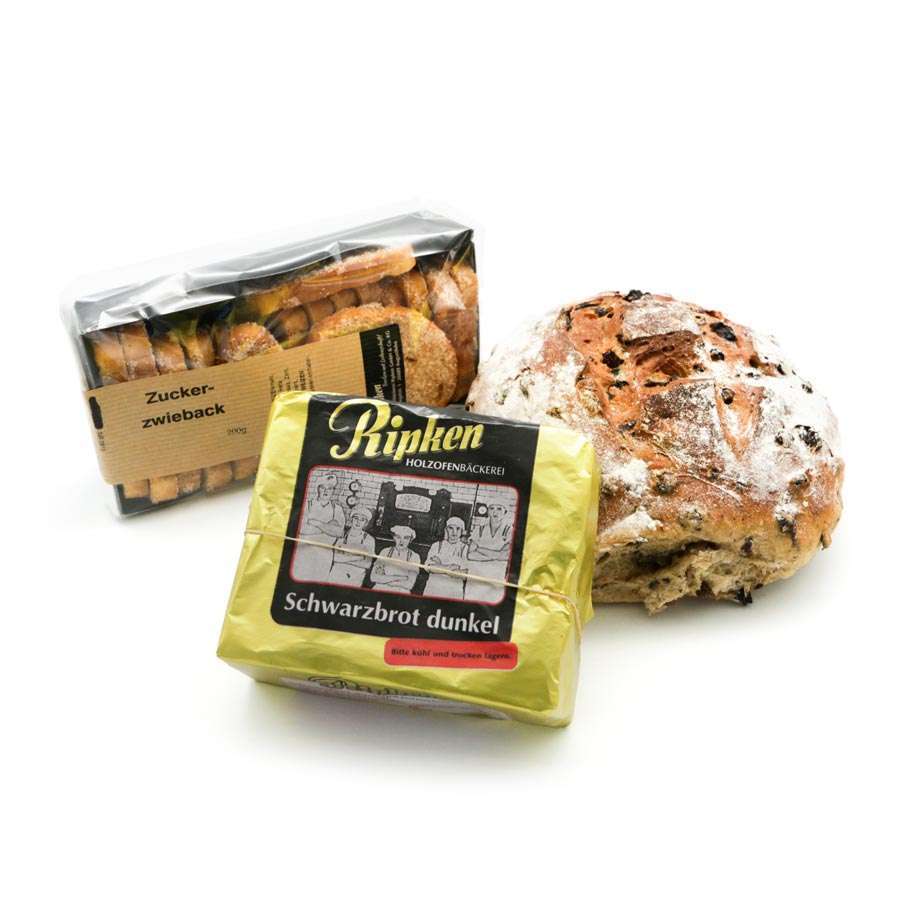Drei Arten von ostfriesischen Backwaren: ein rustikales Korinthstutjes, eine Packung Zuckerzwieback und ein in goldenes Papier eingewickeltes dunkles Schwarzbrot - in Norddeutschland auch als Swartbrood bekannt - sind auf weißem Hintergrund zu sehen.